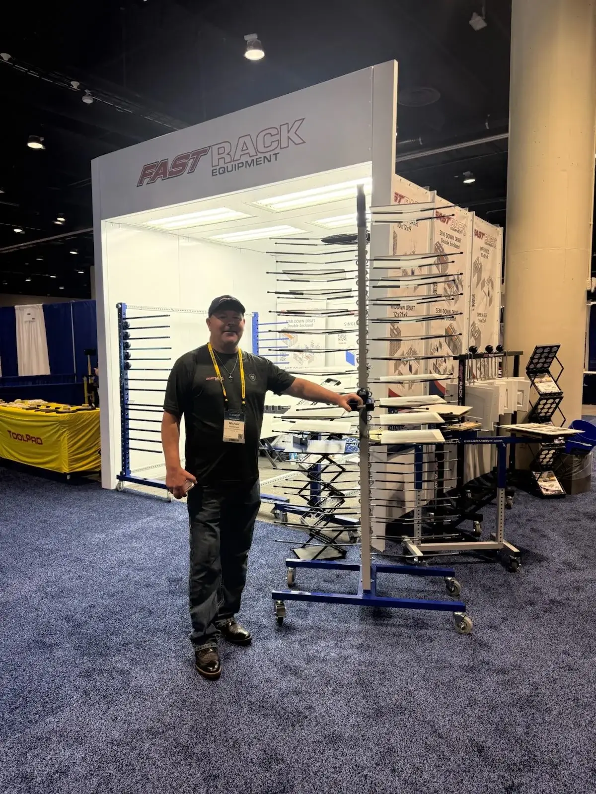 A Fast Rack Equipment trade show display featuring a physical spray booth assembly and custom drying racks for industrial finishing.