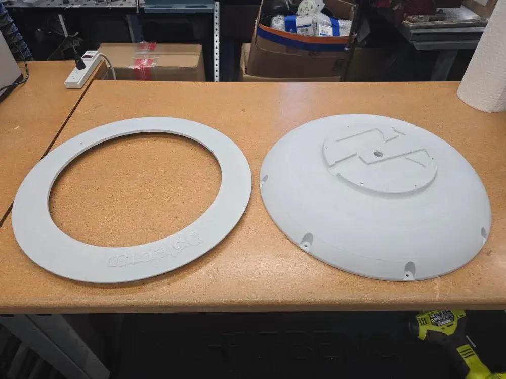 Top view of two 3D printed prototype components for a next-generation LEP high-bay lighting fixture, demonstrating precision mechanical engineering.